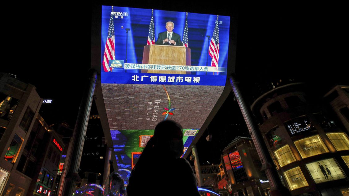 FILE - In this Nov. 8, 2020, file photo, a woman sells balloons near a giant TV screen broadcasting a news of U.S. President-elect Joe Biden delivers his speech, at a shopping mall in Beijing. (AP Photo/Andy Wong, File)