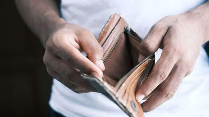 Bildet viser hendene til en person som holder en åpen lommebok. Lommeboka er tom.