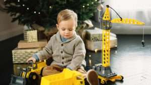 Et barn (en gutt?) som sitter foran et juletre med biler og en heisekran.