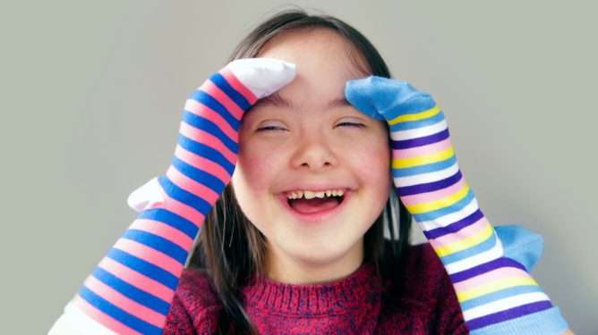 Jente med downs syndrom som har to ulike sokker på hendene. Hun ler.